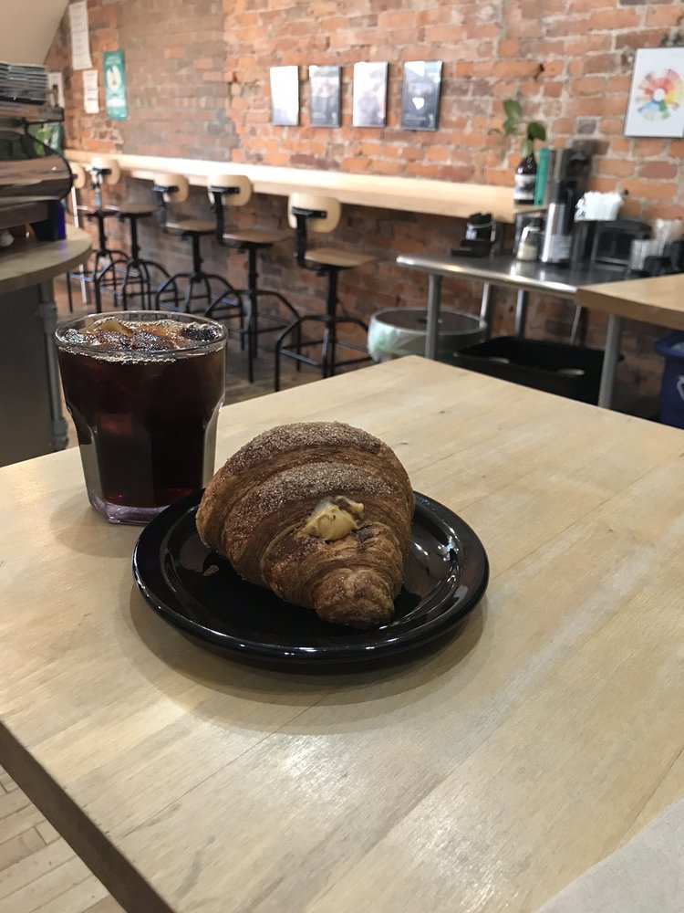 small glass of hand poured coffee with a bakery item on a place next to the coffee.