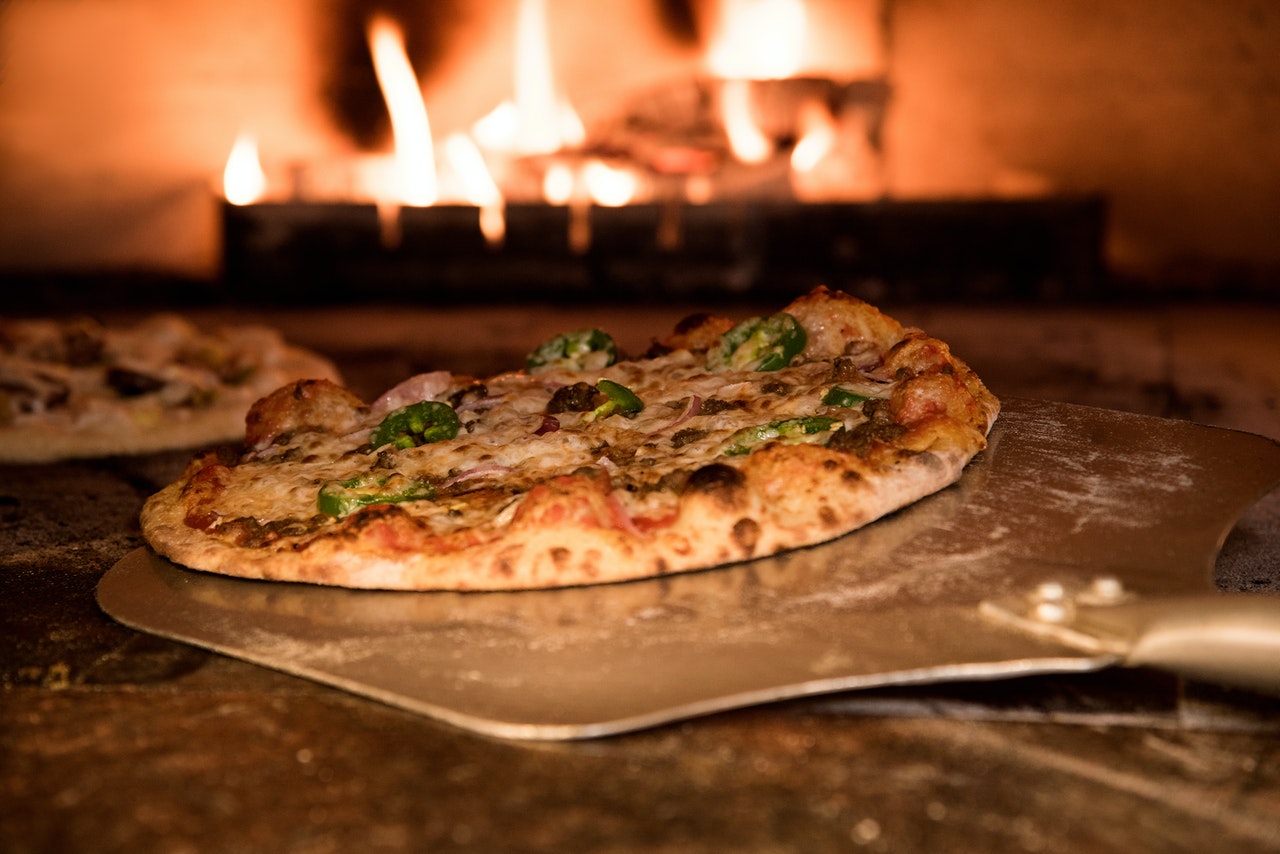 pizza being placed in a stone oven with a peel