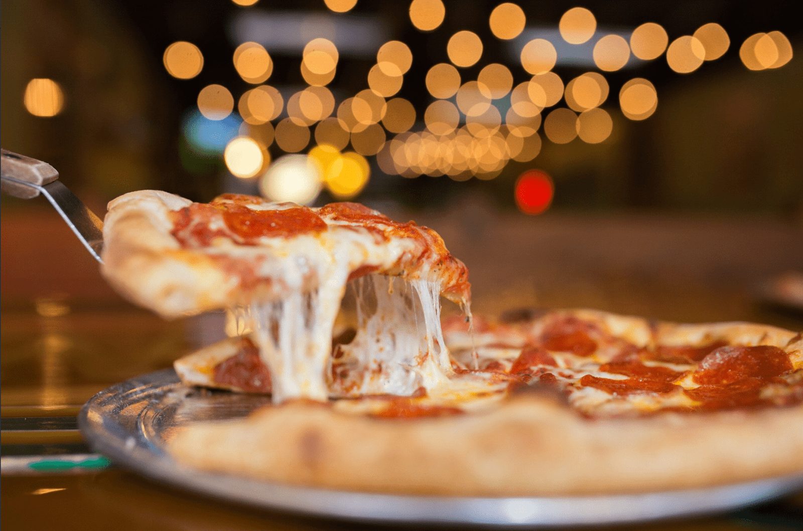 Cheesy slice of pizza being cut out of a pie