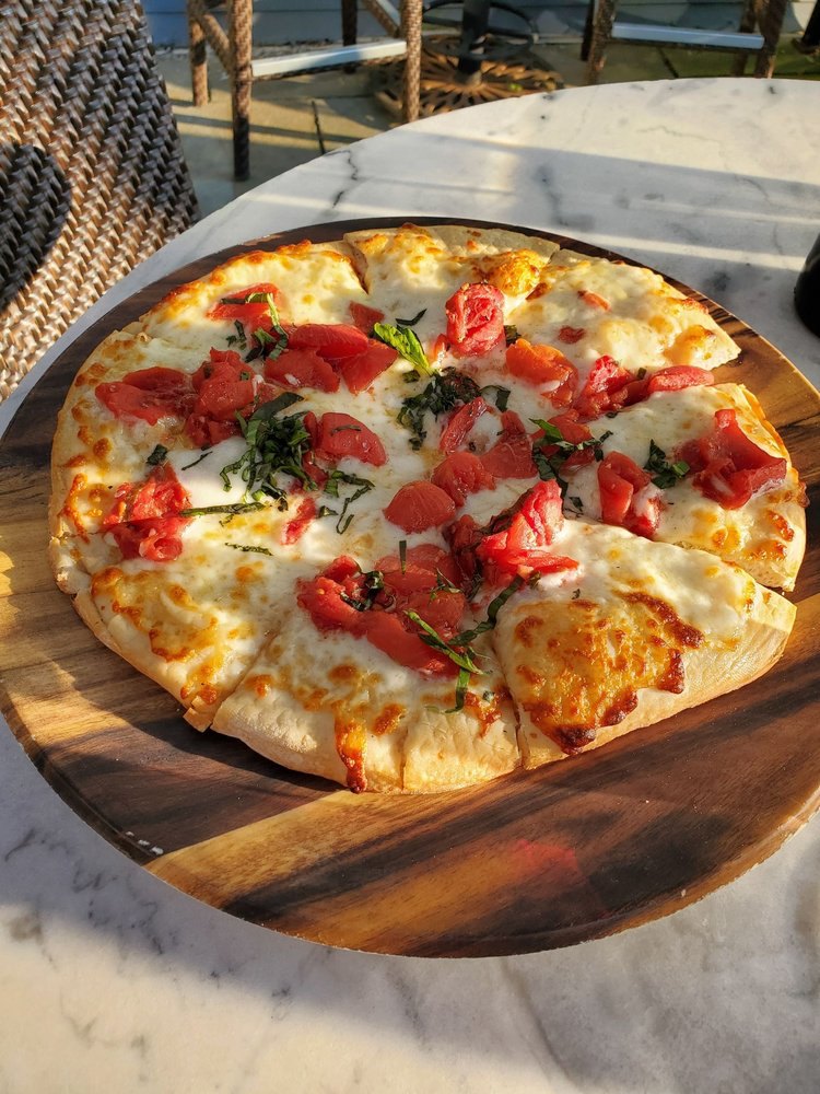 Margherita Pizza on outdoor table. Pizza is topped with cheese, basil, and tomatoes.
