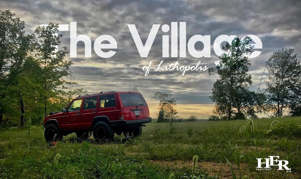 A red SUV ina green field with trees against an orange and blue sunset