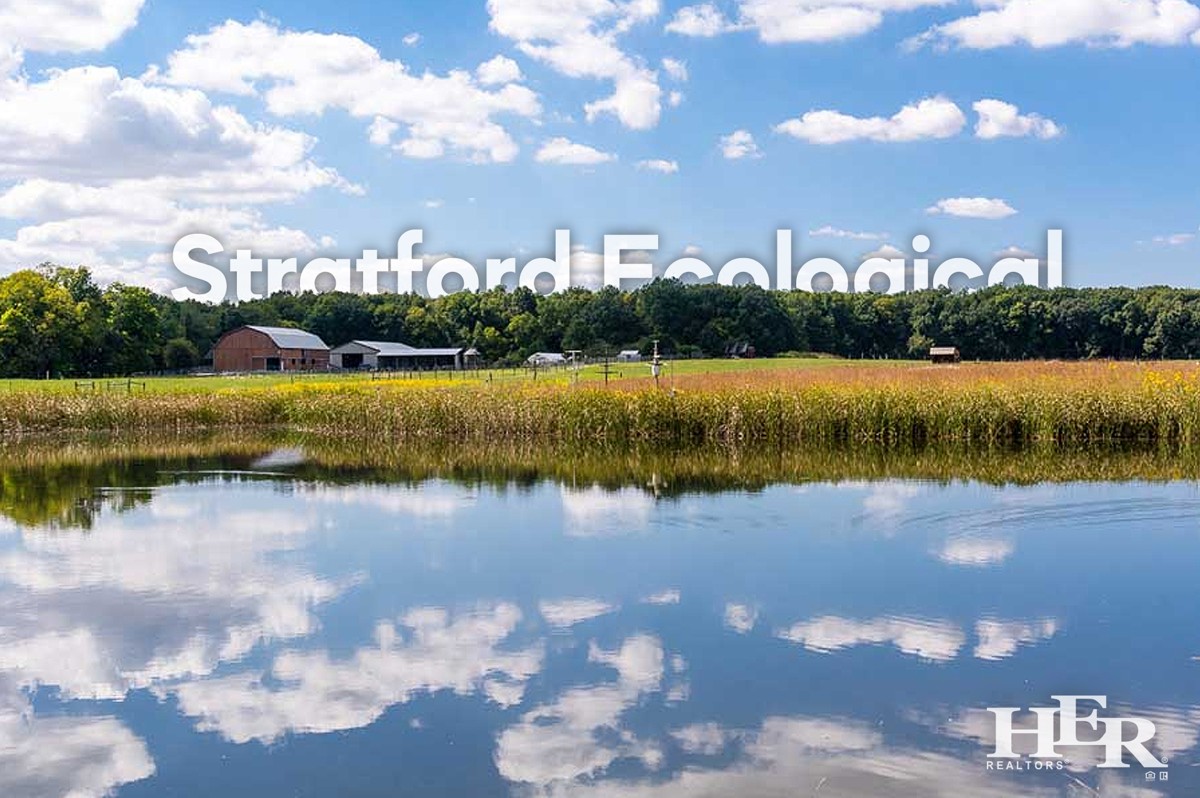 blue lake with field, farm, and forest in the background