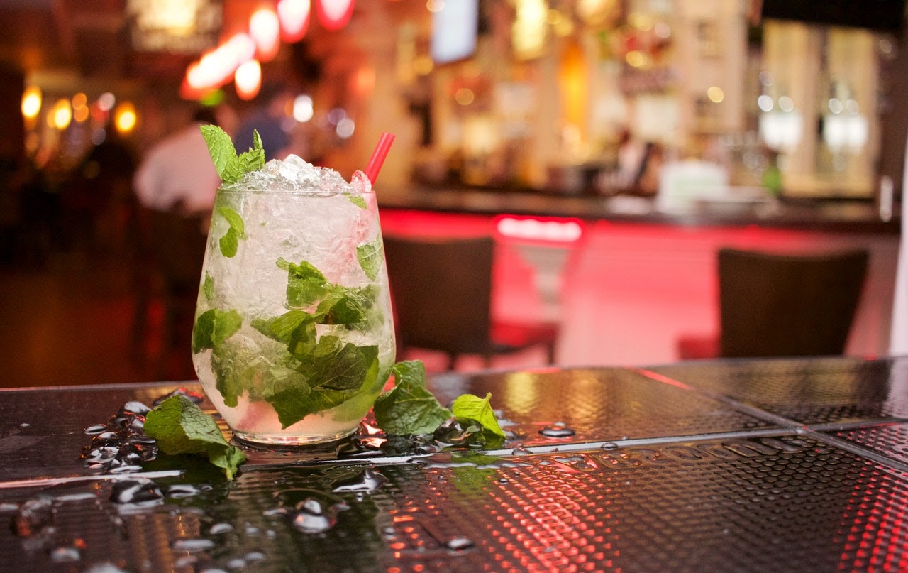 A closeup of a mixed cocktail sitting on a bar top. It's full of ice and mint leaves.