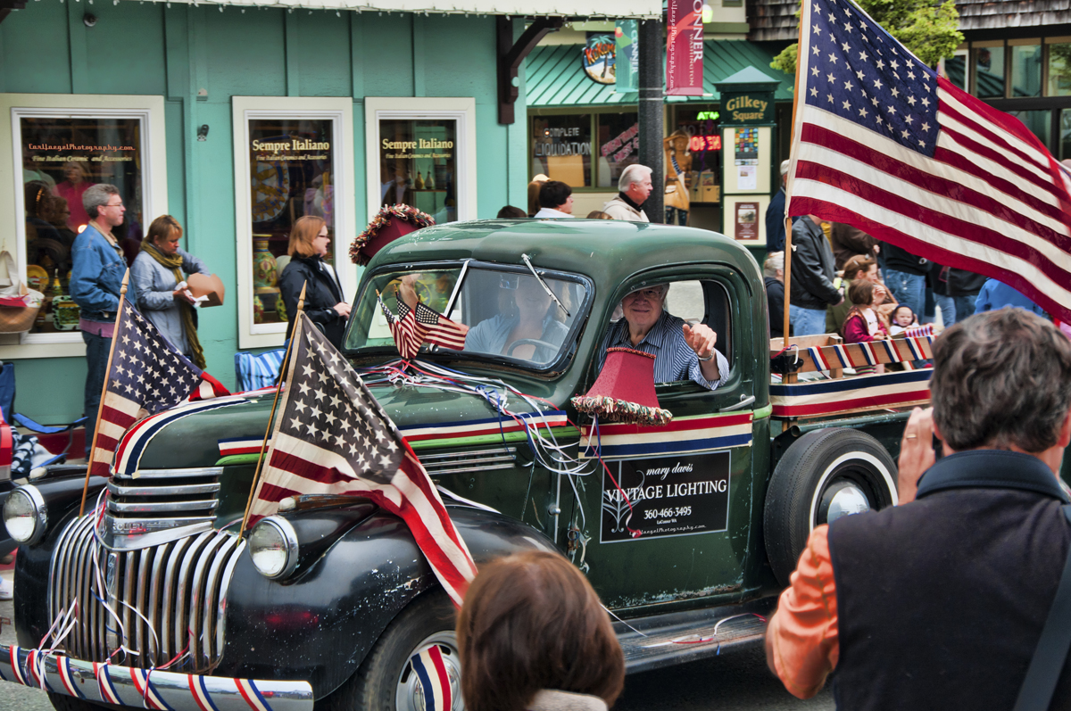 old couple driving green antique car with American flags