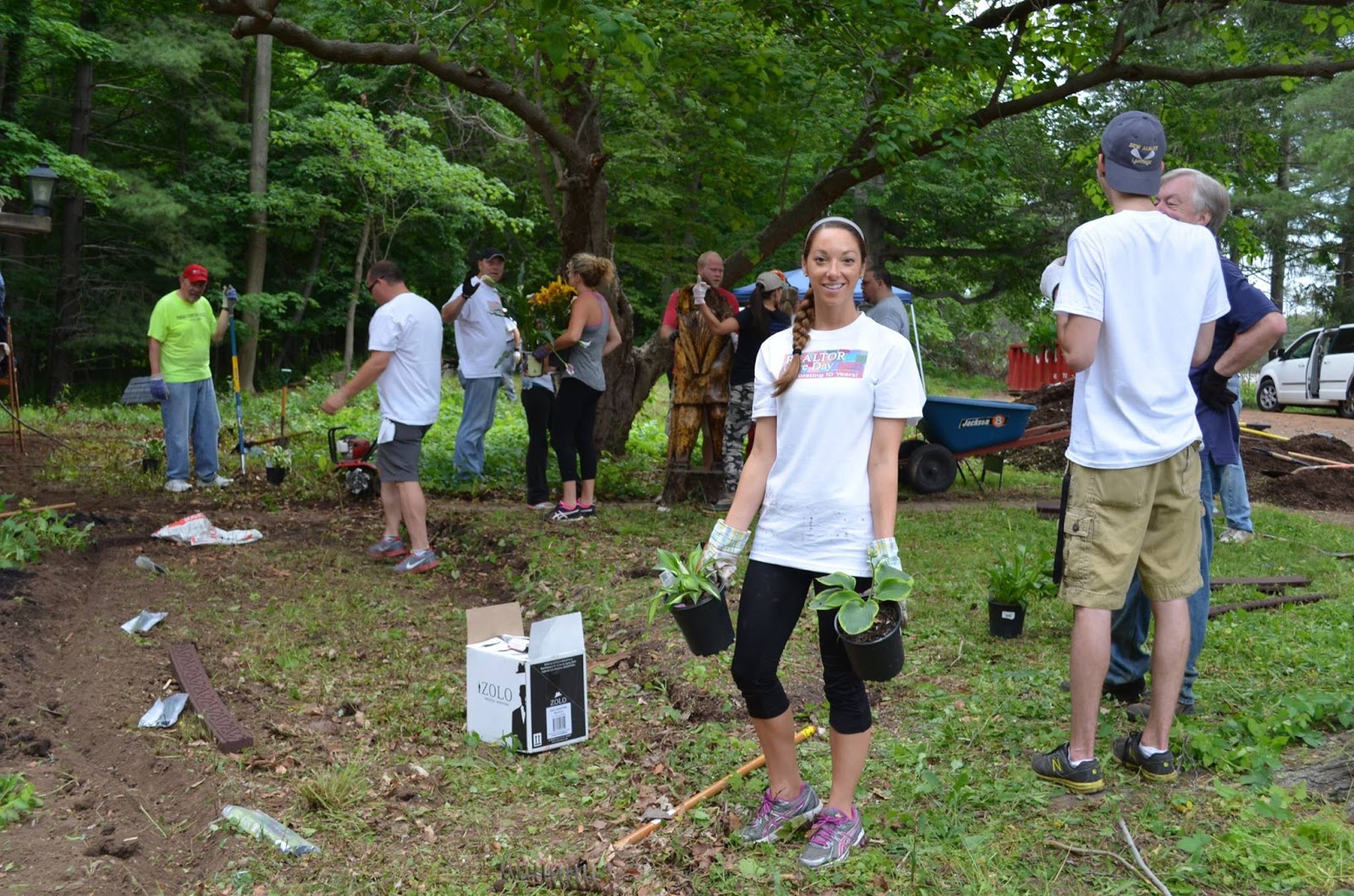 woman carrying two plants with people gardening in the background