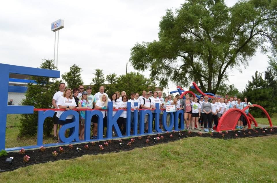 large group of people standing behind large blue Franklinton sign