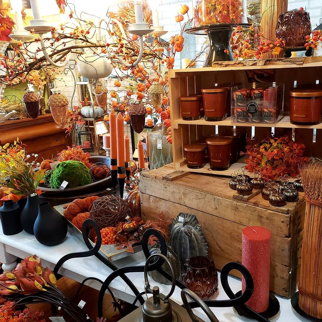 A shelf in Fireplace Gifts And Florist with candles, brass pumpkins, and other kinds of fall decorations.