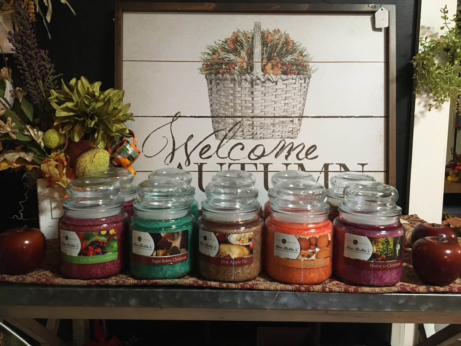 Closeup of a welcome to autumn sign at The Flower Pot. In front of it are five kinds of scented candles.