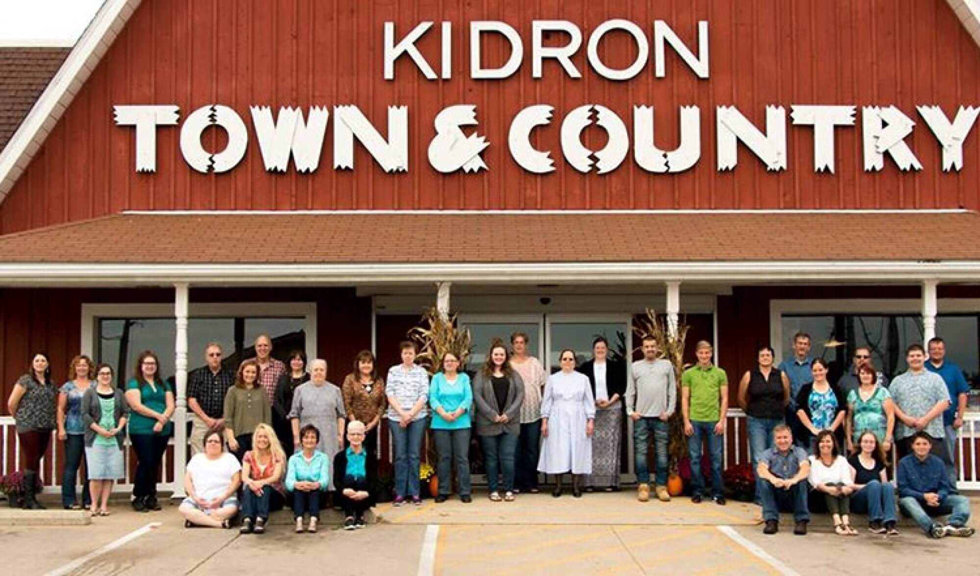 A large group of people stand in front of the Kidron Town and Country store.