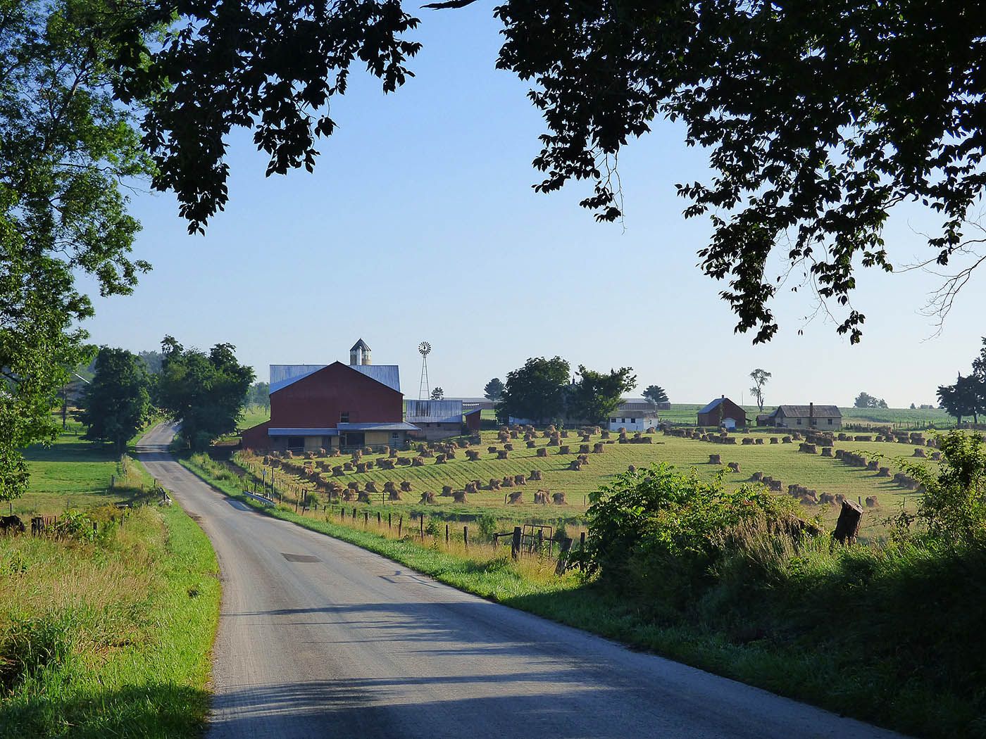 A country road sits next to a farm and a field of hay bails.