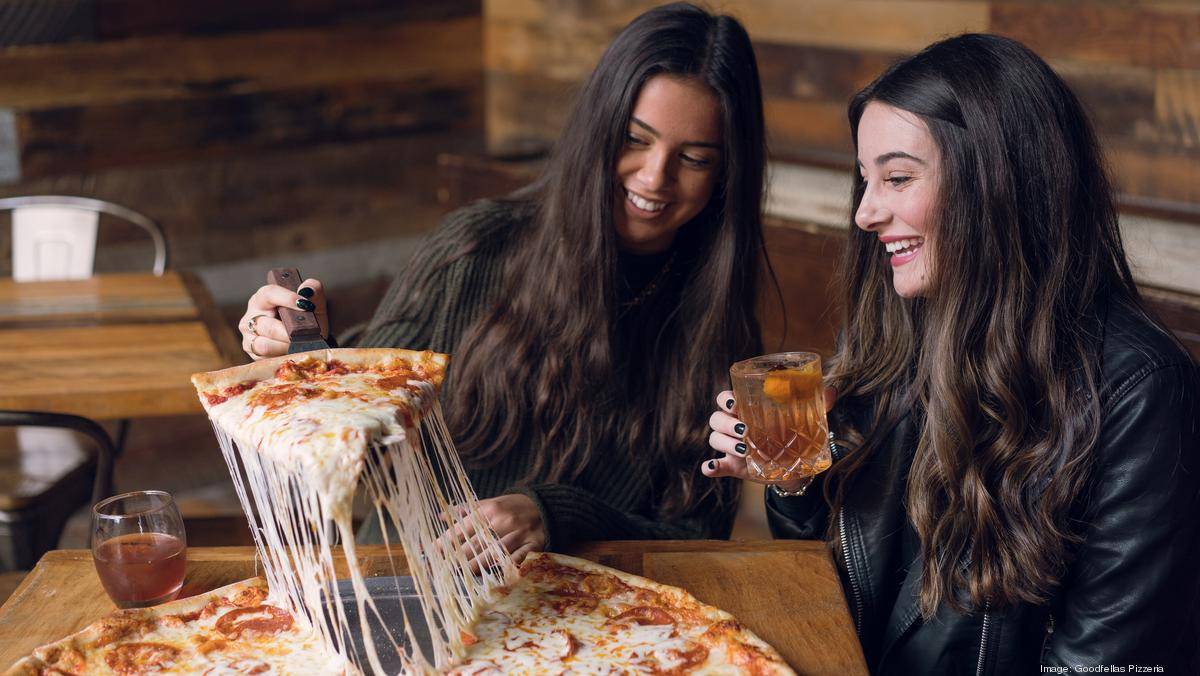 Two girls are eating big Pizza with wine