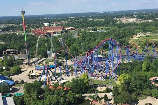 An overhead view of rides at an amusement park surrounded by trees.