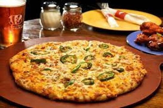 A pizza topped with jalapenos next to wings and a beer.