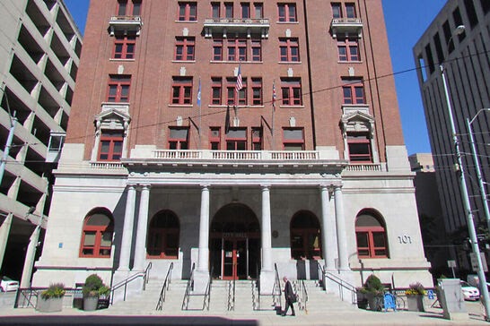 A brown building in between a gray building and a parking lot.