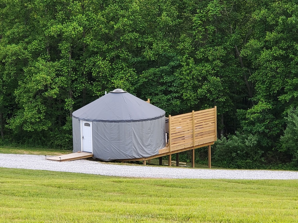 A yurt– a tent-like building– perched on a wooden deck nestled on the edge of the forest
