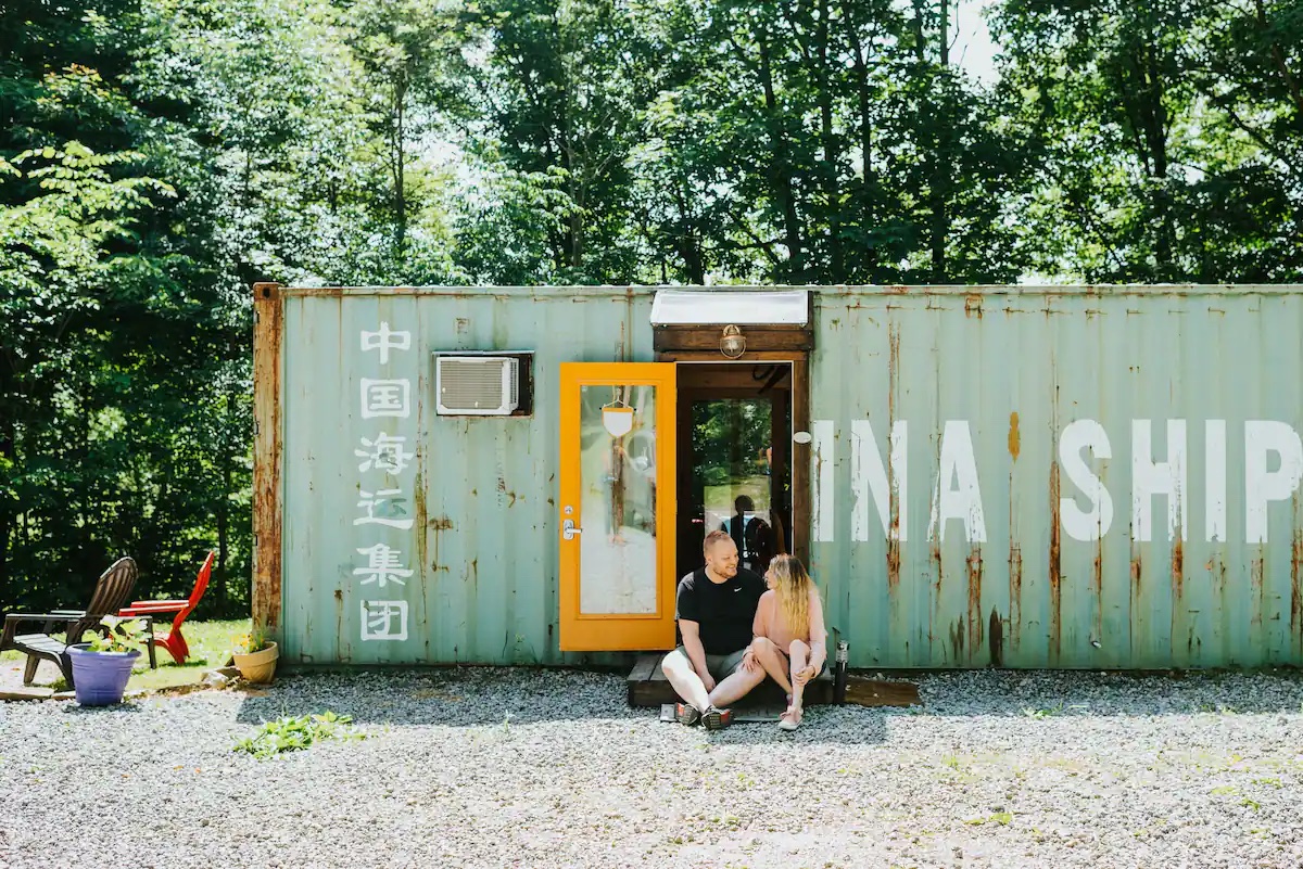 Renovated shipping container with a yellow glass door and a couple sitting in the doorway