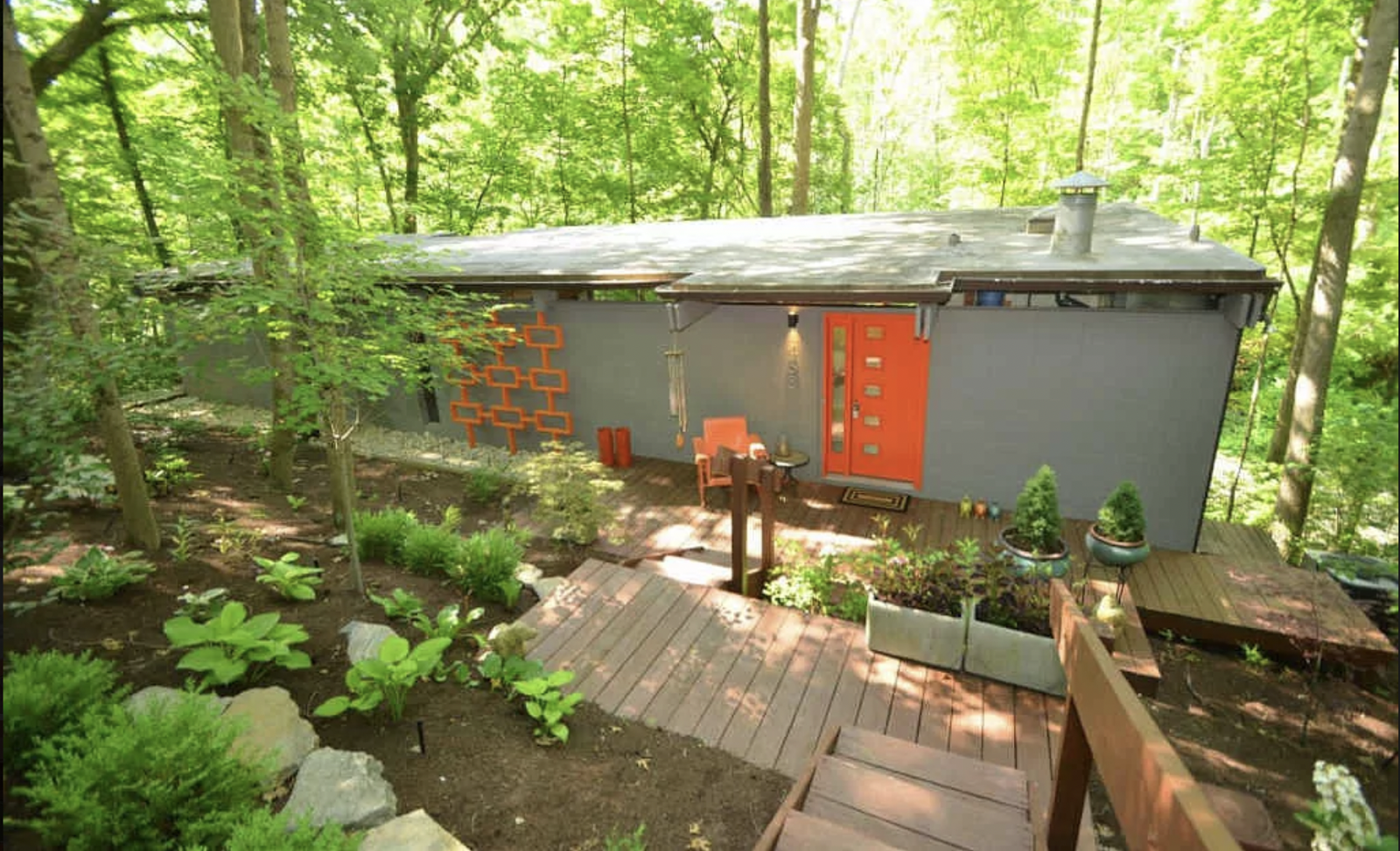 Gray house with orange details and a wooden deck in the forest
