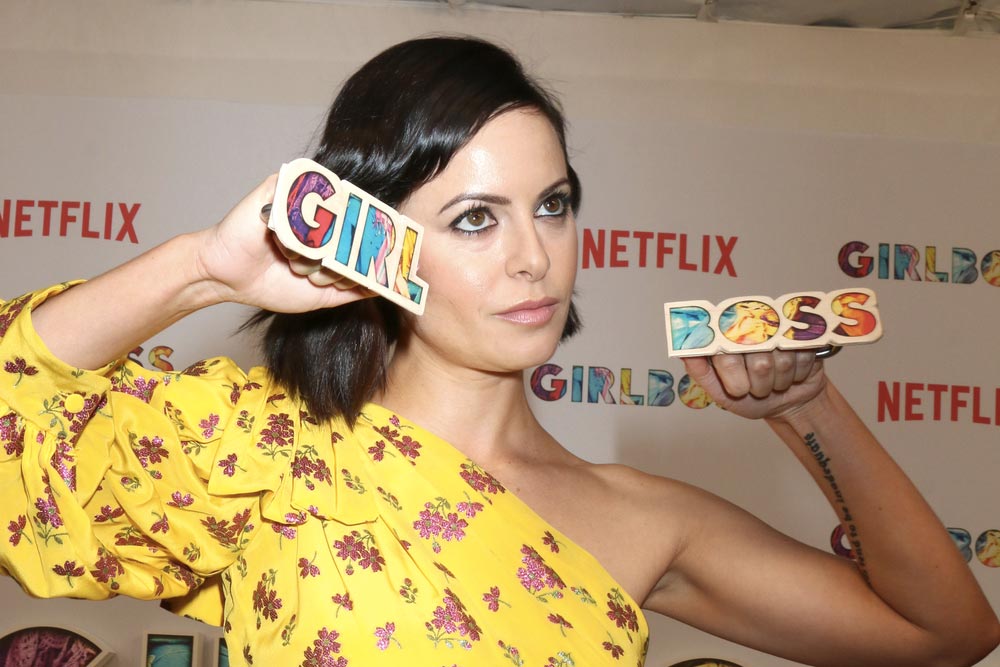 Sevědomá Sophia Amoruso pózující s barevným nápisem GIRL BOSS.