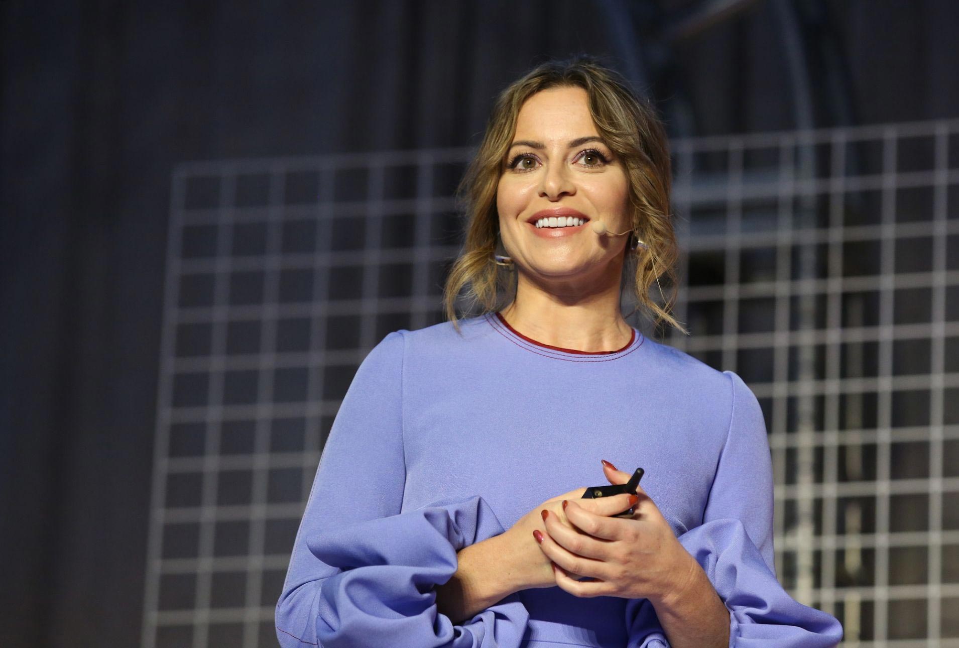 Sophia Amoruso v modrých šatech přednášející na konferenci svému publiku.
