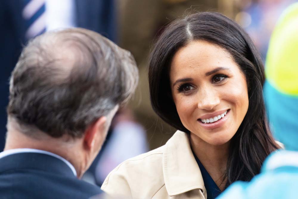 Klidně vypadající Meghan Markle se roztomile dívá na neznámého muže.