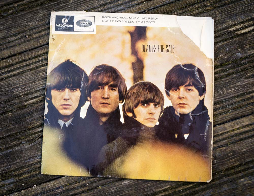 Plakát ležící na černém stole, na kterém jsou vyobrazeni všichni členové slavné kapely Beatles.