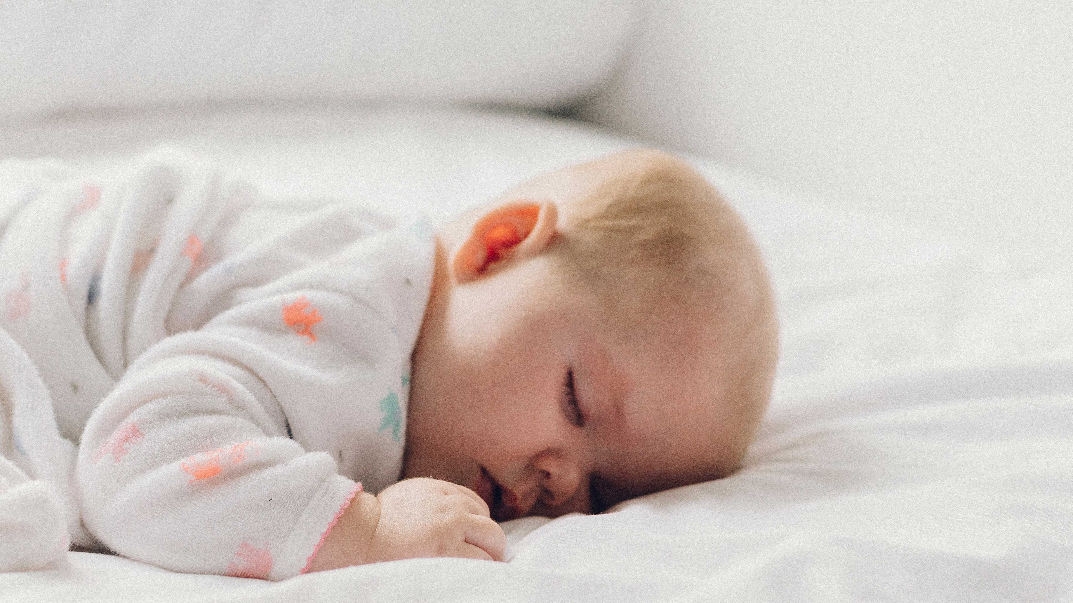 Bebê dormindo com o rosto virado de lado em cama branca