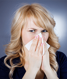 Young woman with possible nasal polyp symptoms blowing her nose.