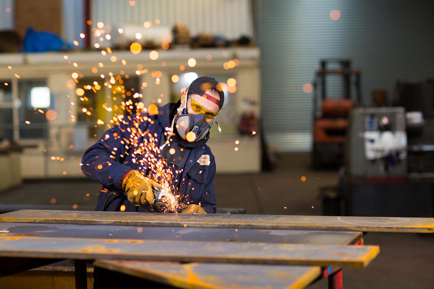 Engineer in welding mask grinding steel with sparks flying