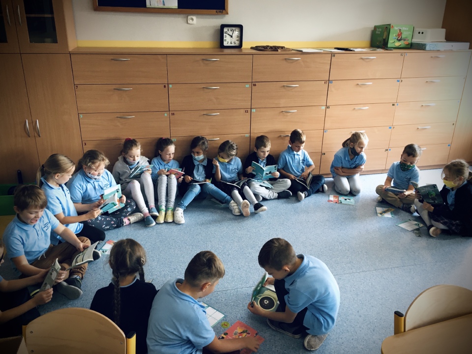 Dzieci z klasy 1 siedzą w kole i czytają lub przeglądają otrzymane książki