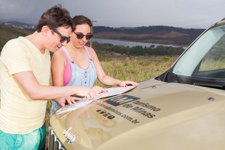 casal olhando um mapa no capô do jeep escrito turismo de Minas