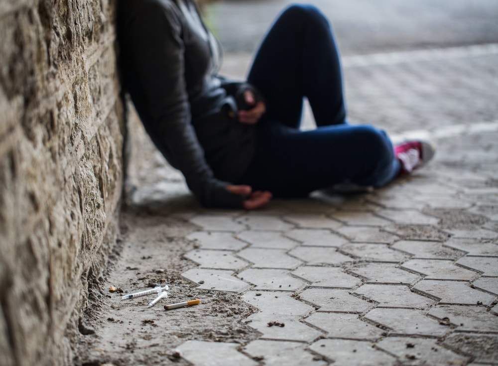 Drugged man sitting on floor in alleyway