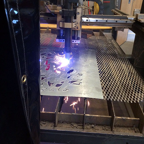 Image of a plasma cutter cutting metal into a typographic skirt.