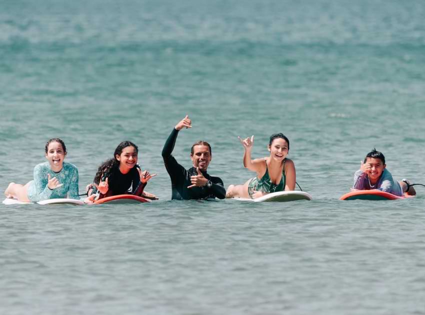 BeachBreak surf instructor with his students smiling at the camera in the water.