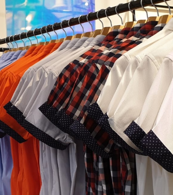 navy polka dotted cuffed short-sleeved dress shirts in various colors hanging on a clothes rack in store.
