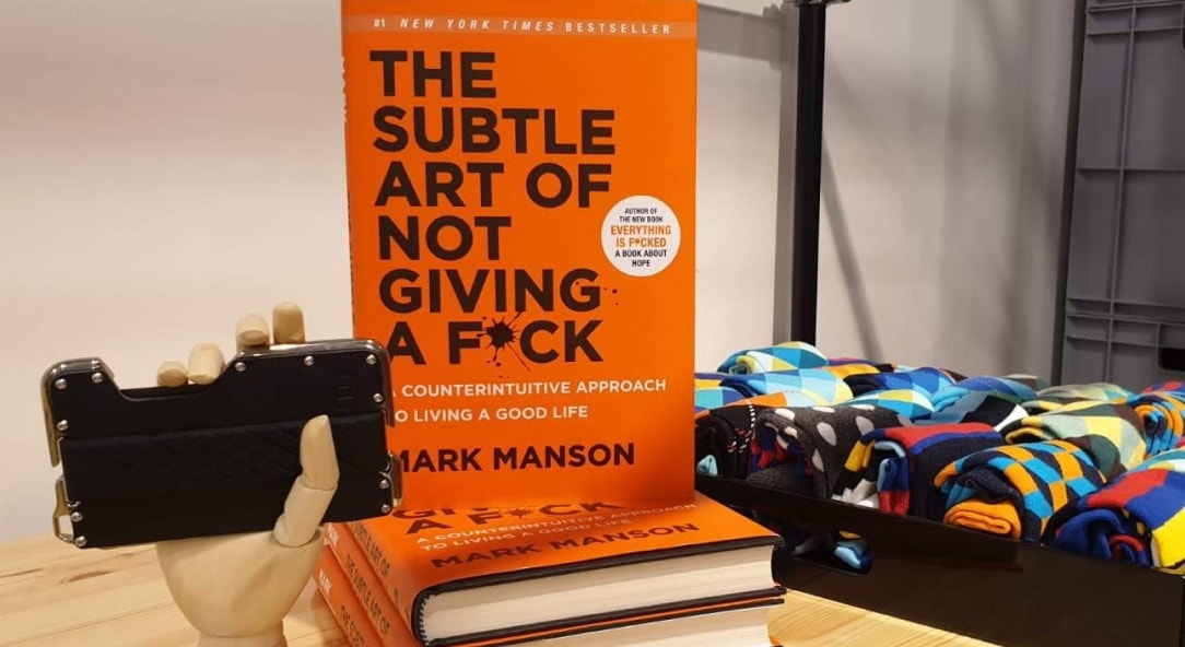 a phone case, a hard cover book "the subtle art of not giving a f*ck", a box of colorful dress socks