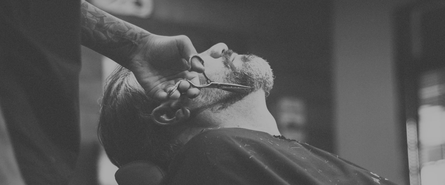 man getting his beard trimmed with scissors in barber chair