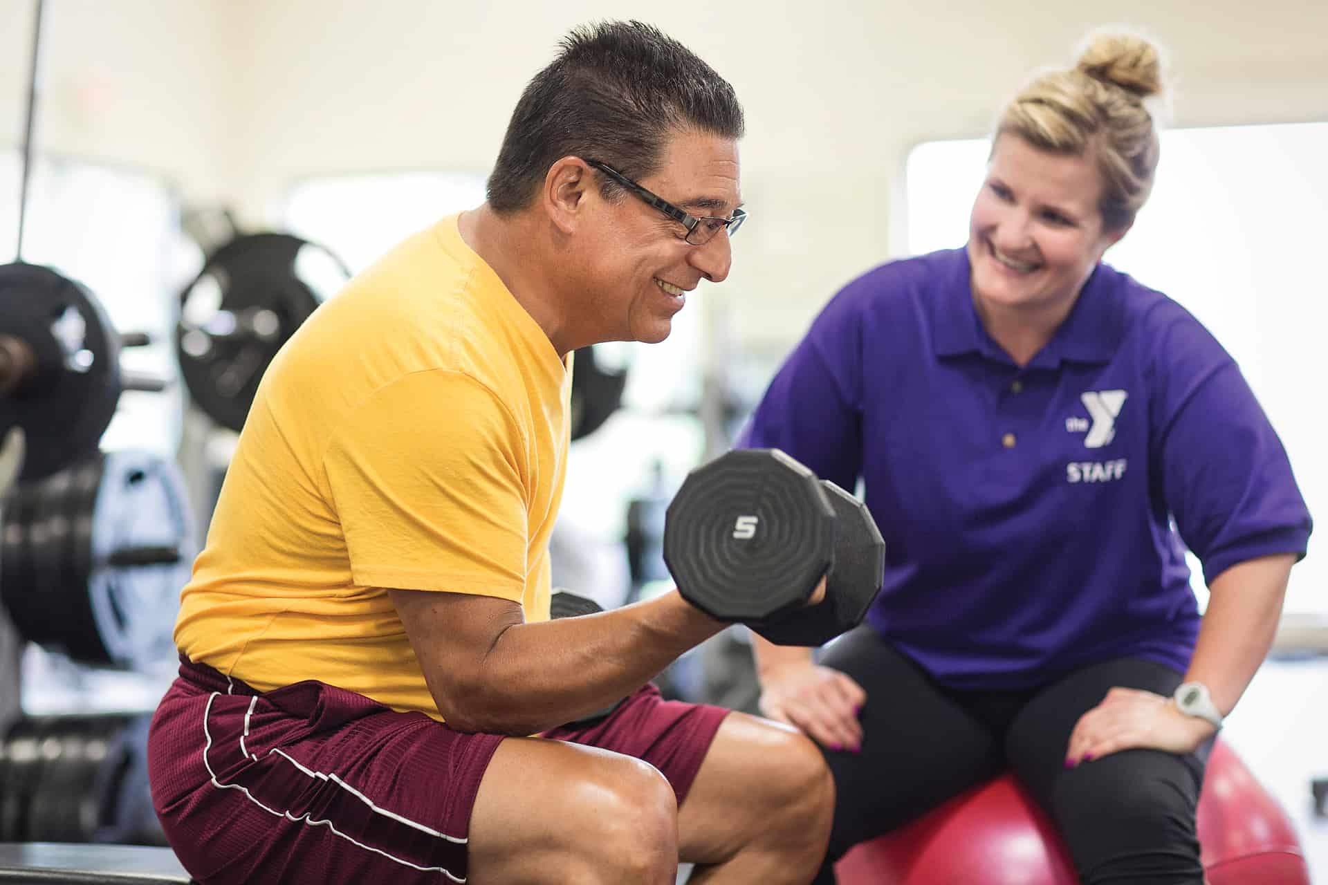 Female trainer teaching proper bicep curl form to an older gentleman.