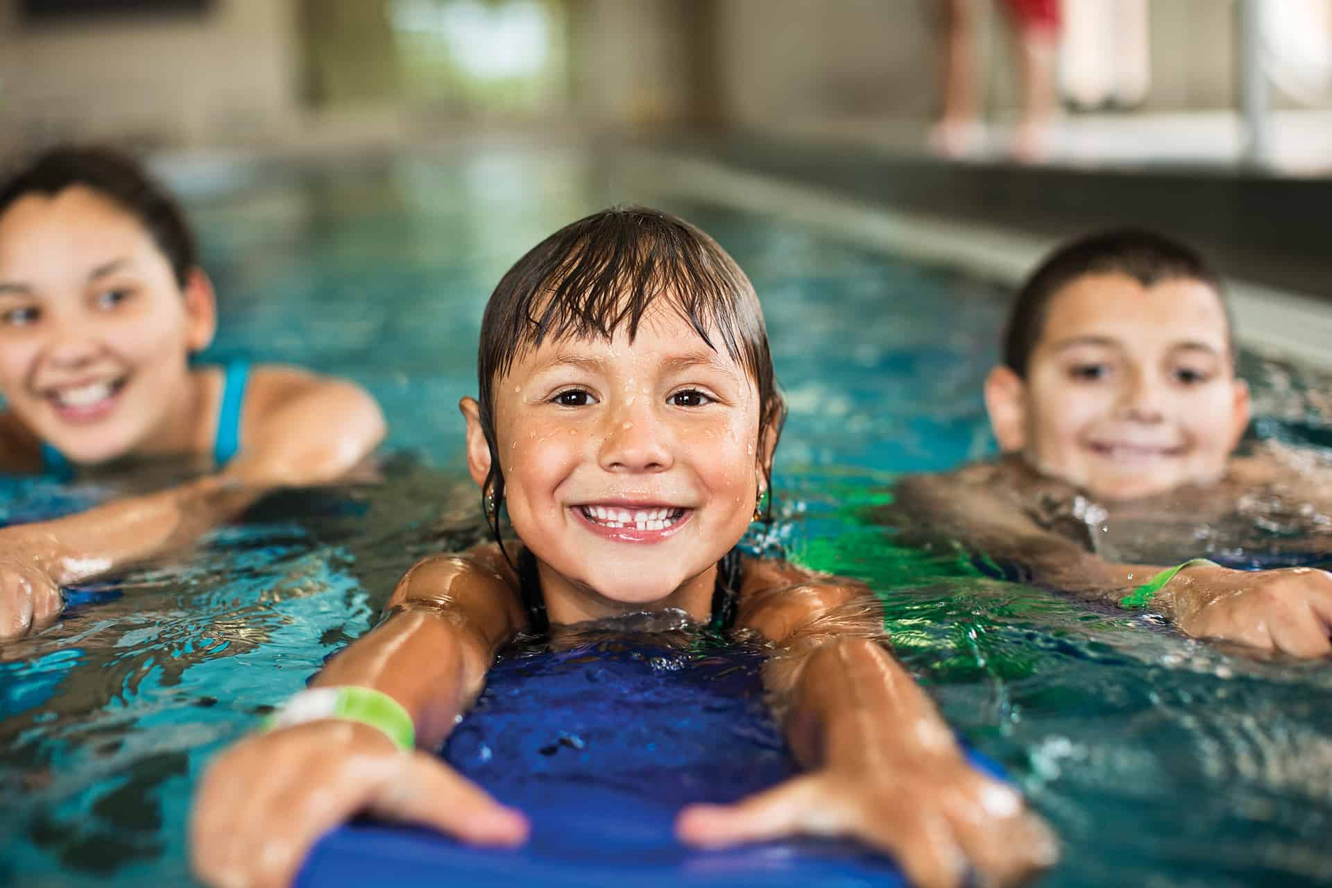 A little girl swimming to her instructor on a kickboard.