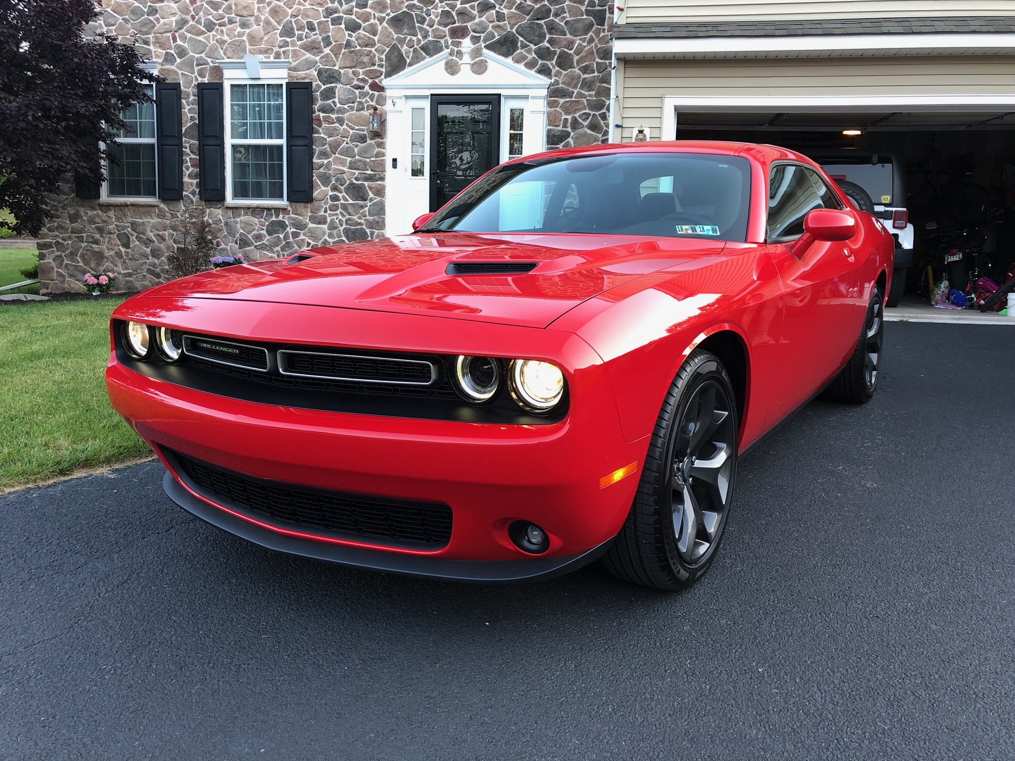 red 2018 dodge challenger parked in the driveway of a suburban home with a stone facade and black shutters