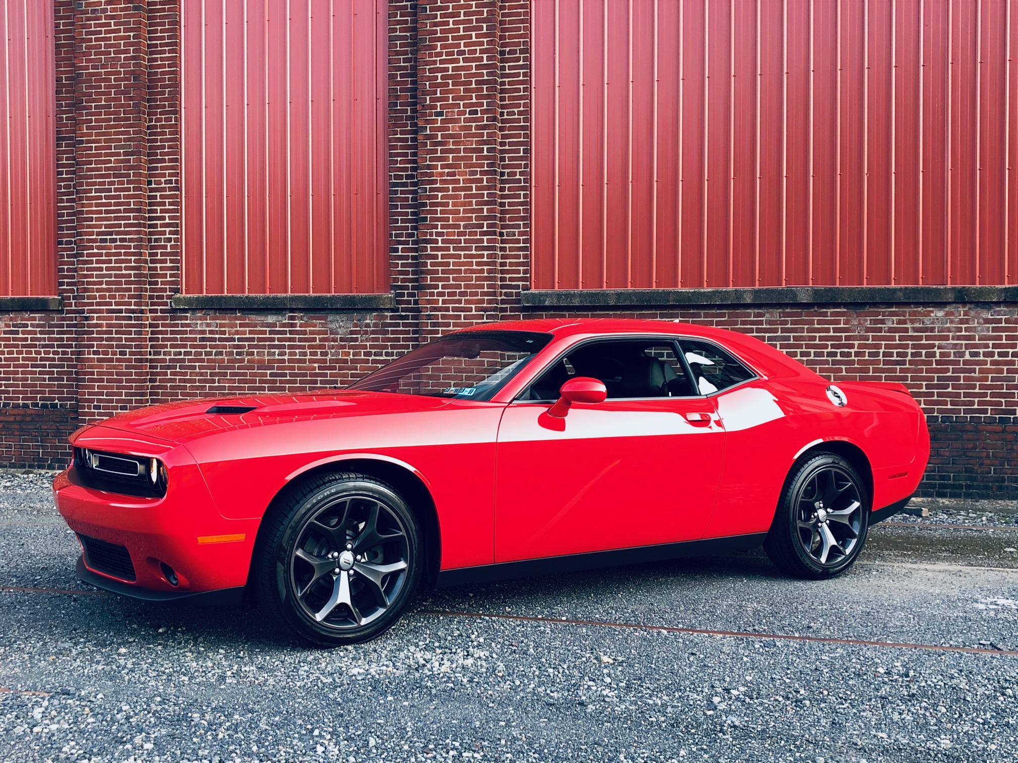 a photograph of a cherry red dodge challenger parked in front of a red brick wall with vertical red paneling