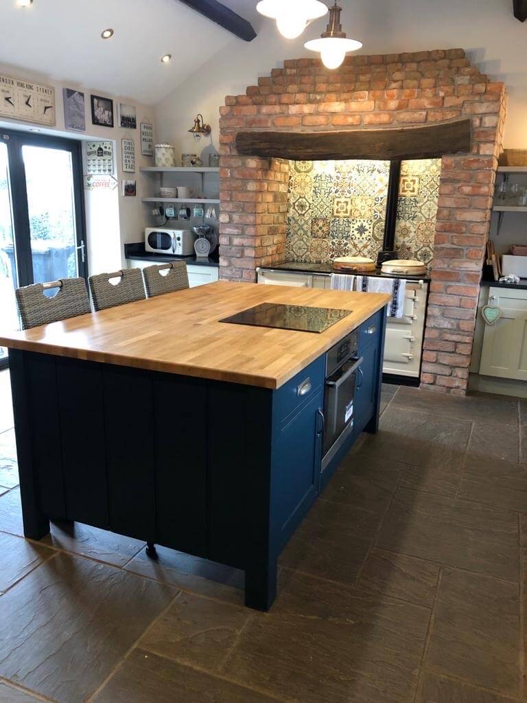 Bespoke painted shaker style large kitchen island with built-in hob and oven with pull out baskets by the seating area.