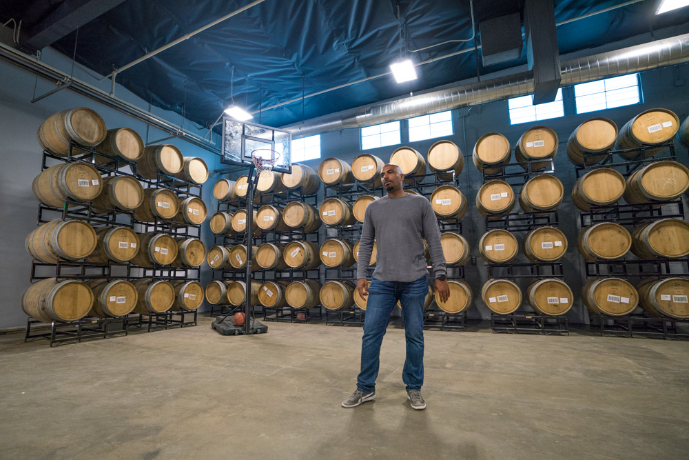 Rob Archie stands in front of casks and smokers at Urban Roots Brewery and Smokehouse in Richmond Grove Sacramento for Visit Sacramento.