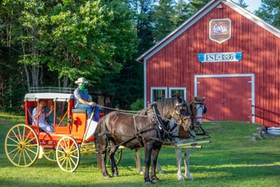 Guests' sit in an 1850s Henderson Stagecoach pulled by draft horses in front of the original 1886 Stagecoach Barn at the Lake Clear Lodge & Retreat.