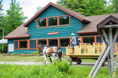Lucky Clover Farm Horses Jasper and Fly pull a Pioneer Wagon in front of the Lake View Great Camp at the Lake Clear Lodge & Retreat.