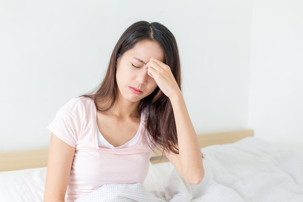 Young woman sitting on edge of bed, experiencing sinus pressure between her eyes.