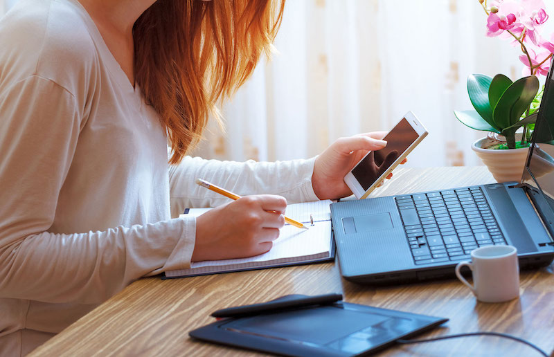 Woman referring to her phone and laptop for content to write