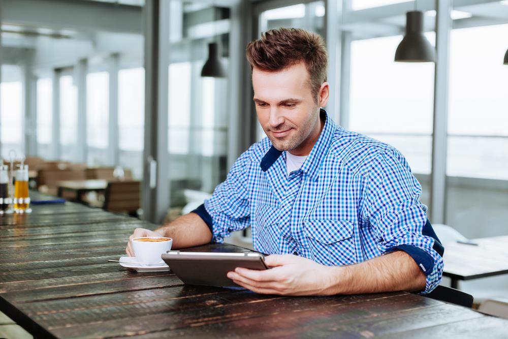 A man drinking coffee and looking at his electronic device