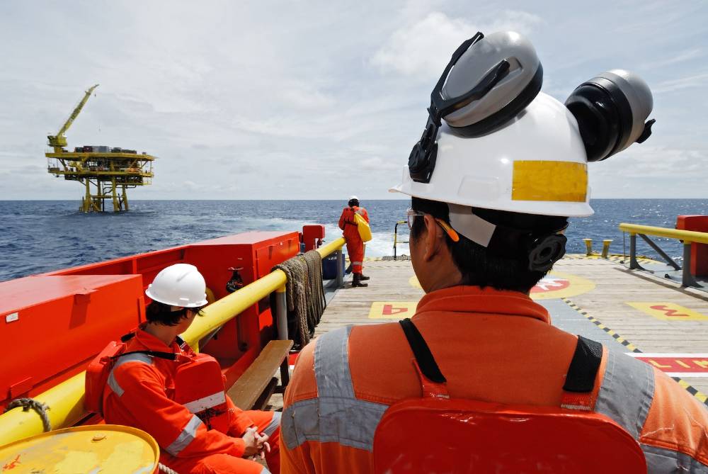 Three people onboard a vessel on the water looking at an offshore marine facility