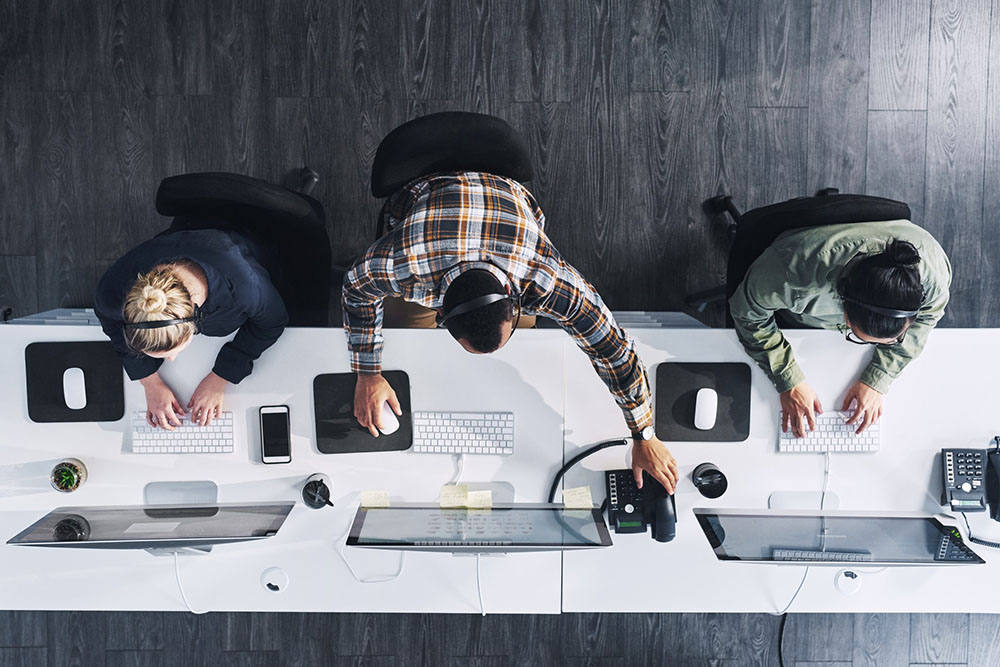 Overhead shot of three technology consultants working at a long desk.