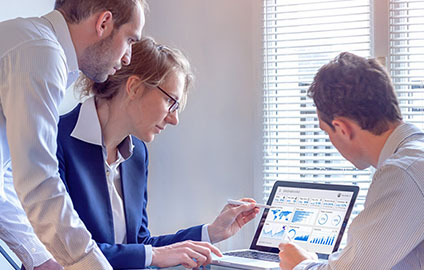 A group of three business people surrounding a computer and looking at key performance indicators on a dashboard.